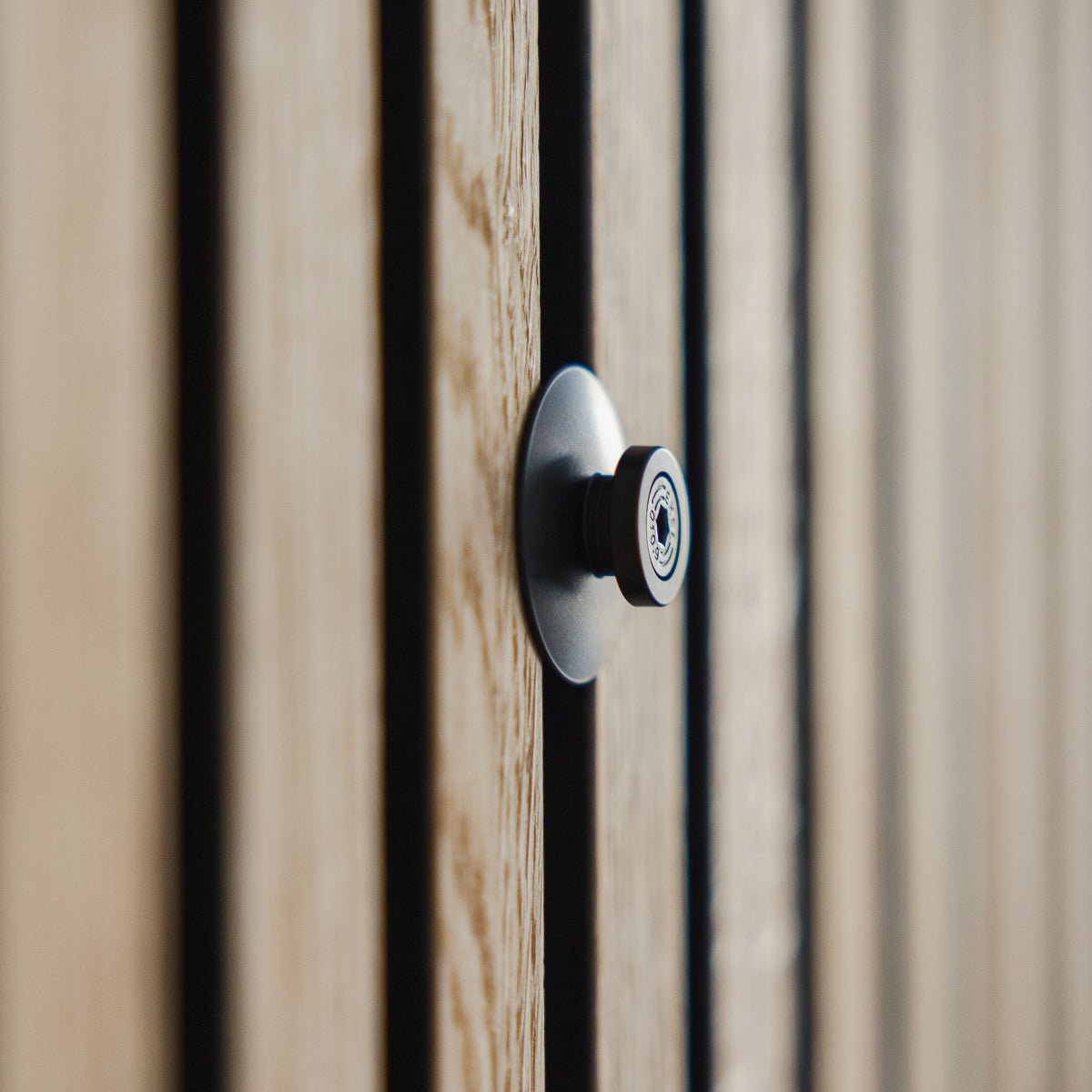 Nærbilde av Dupps | Heavy kikkehull fra WoodUpp i black aluminium, montert på en rillet tredør med Akupanel akustiske lameller, med linsen i fokus.